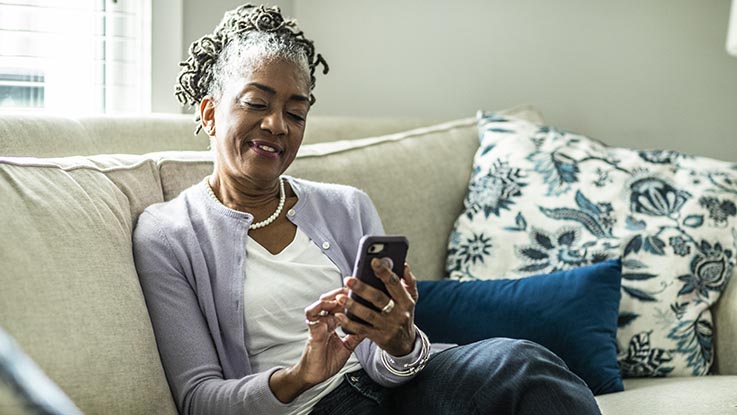 A woman sits on her couch as she uses her smartphone